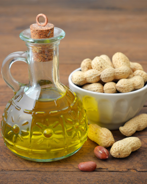 Eine Flasche mit Erdnussöl auf einem Holztisch, umgeben von Erdnüssen – ein nährstoffreiches Öl, das in der Kosmetik für Haut- und Haarpflege verwendet wird.